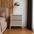 Beige nightstand next to a bed with a textured wall and lamp in the background