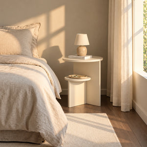 Cream round end table beside bed with lower shelf