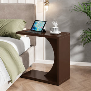 Dark brown C-shaped end table beside a bed