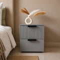 Grey Solid Wood bedside table with fluted drawer design and black handles placed beside a modern bedroom bed.